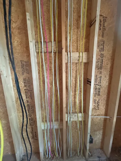 Rows of white and yellow electrical cable stapled neatly up a framed wall between engineered studs