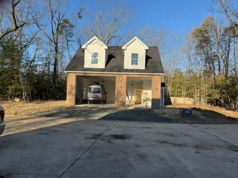 The finished carriage house from the front: two dormers over two open garage bays between brick piers, at the end of a paved drive