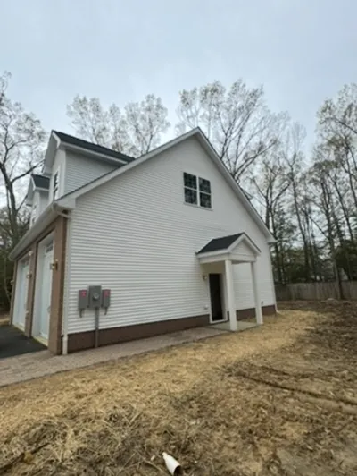 The finished carriage house from the side: white siding over a brick base, a covered side entry and the electric meter on the wall