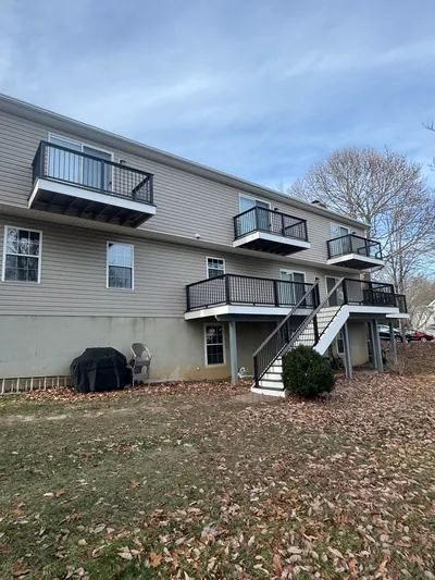 The back of a house with three balconies above a deck, all with black railing, and stairs down to the lawn