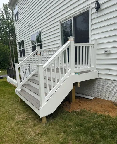 White steps and railing climbing to the sliding back door of a white-sided house, with gray composite treads and a lantern light beside the door