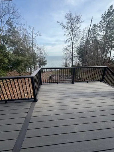 A composite deck with black railing, looking through bare trees to open water