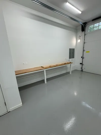A finished garage bay: gray epoxy floor, a long butcher block workbench, a panel on the wall and strip lights overhead