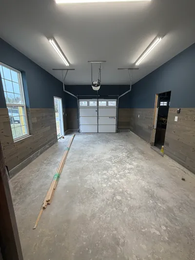 A finished garage: dark blue walls over wood plank wainscot, strip lights, a side window and a white overhead door