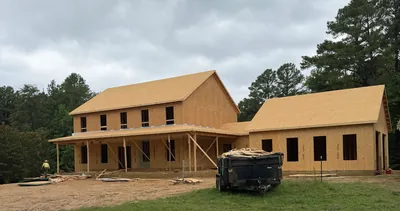 A two-story home and its garage wing framed and sheathed in plywood, the front porch roof held on temporary braces