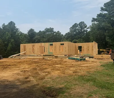 The first-floor walls of a new home standing on its foundation, seen across the cleared lot