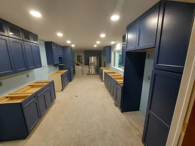 A long kitchen in the middle of a remodel: navy cabinets set along both walls, recessed lights on, countertops still to come