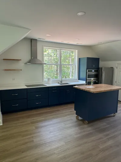 The loft kitchen: navy cabinets, a butcher block island on casters, a steel range hood and a wide window over the sink
