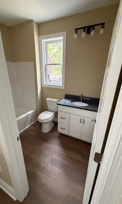 A full bathroom in the pool house: a white vanity with a dark stone top, a tub and shower, and a four-light fixture