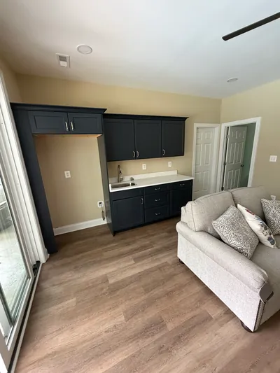 Inside the pool house: a kitchenette with dark cabinets, a white counter and a bar sink, beside a sofa
