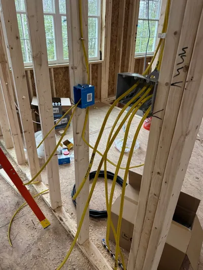 Yellow cables pulled through open stud walls into a gray multi-gang box and a blue device box, with a red ladder at the left