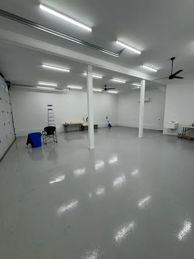 The finished workshop level: a glossy gray epoxy floor, white walls and posts, rows of strip lights and two ceiling fans